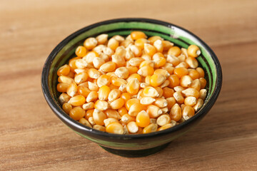 Bowl with yellow corn kernels on wooden table. Raw ingredient closeup. Healthy vegetarian food. Agriculture crop detail. Organic cooking product.