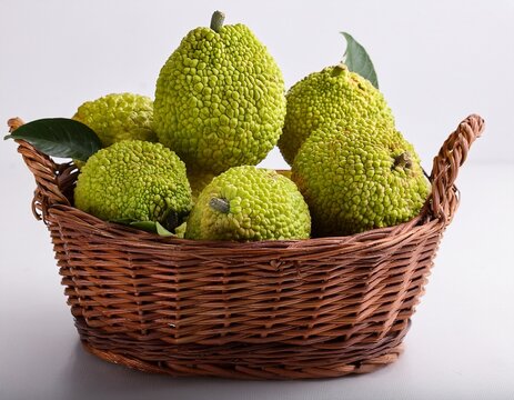 close up view of osage oranges in a brown wicker basket on white background