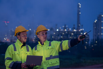Engineers collaborate at dusk near an industrial facility while managing operations and communicating through radio devices