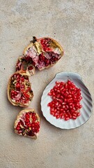 Loose pomegranate (Punica granatum) seeds in a white ceramic plate shot on a wood table. There are pieces of ripe pomegranate fruit around it. Pomegranates are a super food.