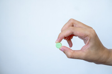 A hand is holding a single small green round pill between thumb and forefinger against a plain white background, emphasizing medication and healthcare