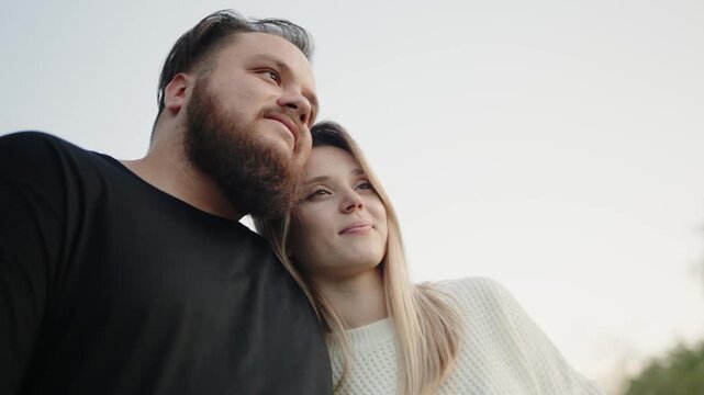 A young couple in a tender embrace, looking into the distance. The image captures a sense of love and companionship in a serene outdoor setting. Young Couple Enjoying a Romantic Moment Together