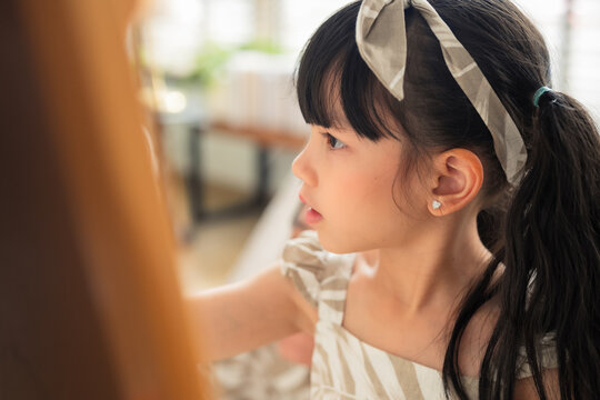 Happy Asian family spending quality time together at home. Father and daughter drawing on the floor with colored pens while mother works on a digital tablet smartphone on the sofa. Warm, modern living - Powered by Adobe