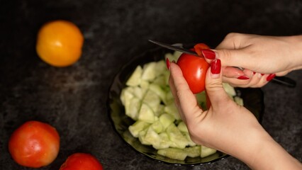 Woman chopping tomatoes on chopped cucumbers