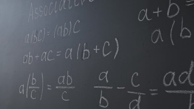Close-up tilt-down shot of black chalkboard with mathematical equations in classroom