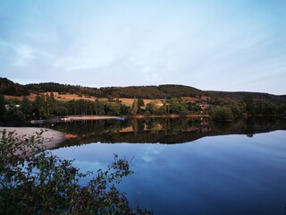 Fototapeta premium Ruhige Abendstimmung am Edersee im September, mit sanften Hügeln, spiegelglattem Wasser und Blick auf den Campingplatz. Naturidylle und friedvolle Atmosphäre. Copyright Sarah Bömer. 