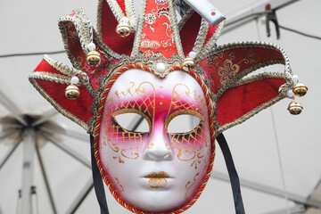Hanging ornate Venetian carnival mask with elaborate red velvet headdress, golden bells, and intricate decorative details. For luxury events, cultural celebrations, and elegant festivities.
