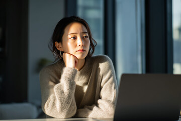 窓の外を眺めながら考え事をする若い日本人女性