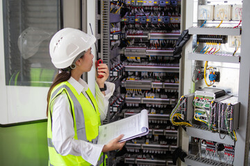 Worker electrical inspection at power plant checking control panel with radio communication and checklist for safety and maintenance in industrial environment
