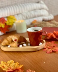 A warm breakfast setting features freshly baked croissants, a steaming cup of coffee, and vibrant autumn leaves. The cozy atmosphere invites relaxation and enjoyment of the season