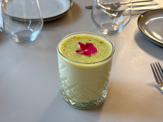 Glass of green matcha drink with edible flower. Refreshing beverage, garnish and modern presentation in cafe setting.