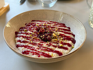 Bowl of creamy oat pudding with raspberry sauce and crushed pistachios served on table. Dessert, sweet food, and culinary creativity in modern dining concept.