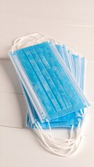Stack of light-blue disposable face masks on white wooden surface