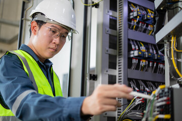 Electrician working on electrical panel with wires wearing safety helmet and vest focused on task in industrial setting