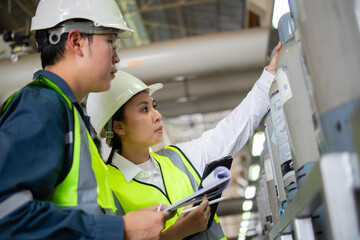 Two engineers wearing safety helmets and reflective vests inspect gas cylinders at power station while checking insulation and taking notes for safety and maintenance