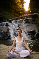 Young woman sitting in lotus pose under tropical waterfall meditating with calm strength and mindfulness fully connected to nature energy tranquility and inner balance
