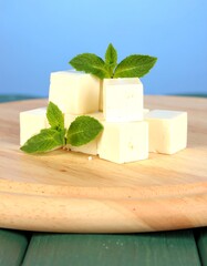 Cubes of white cheese, stacked on a wooden cutting board, with fresh mint leaves