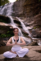 Young woman sitting in lotus pose under tropical waterfall meditating with calm strength and mindfulness fully connected to nature energy tranquility and inner balance