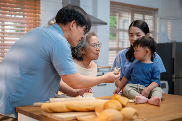 Asian family preparing food together in a cozy kitchen a father slicing bread while the mother and child watch joyfully, surrounded by three generations.