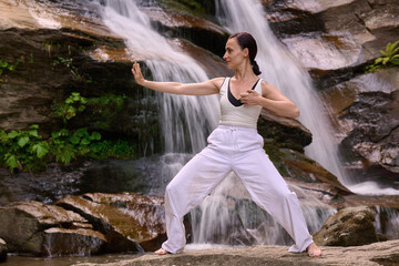 woman performing slow tai chi movements near a waterfall and river at sunset capturing harmony balance and fitness in nature
