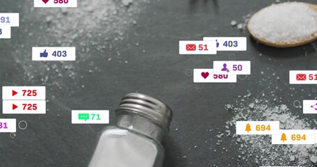 Tilting salt shaker pouring crystals across dark slate surface, with spoon and notification icons