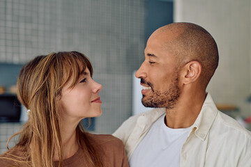Fototapeta premium Young multi-ethnic couple smiling and gazing at each other in their stylish modern kitchen, sharing moments of love and connection