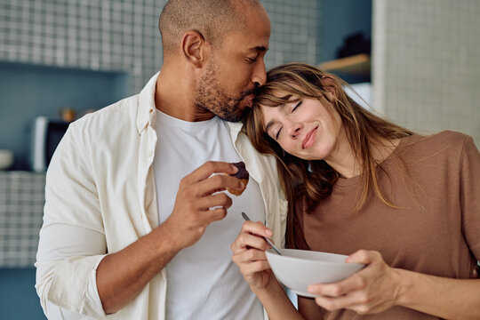 Happy couple sharing a cozy breakfast at home, kissing while enjoying healthy food and savoring moments of love and togetherness