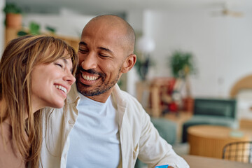 Happy multi-ethnic couple smiling and embracing in their modern living room, enjoying a moment of affection and togetherness