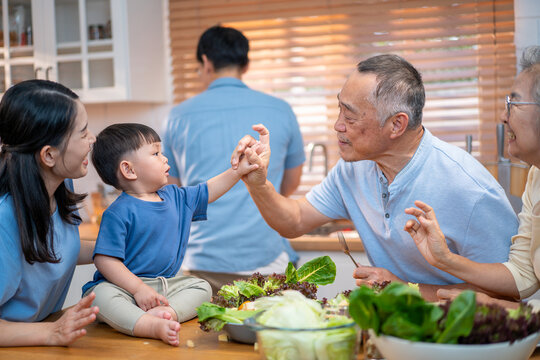 Asian family spending quality time together in the kitchen, preparing healthy meals with fresh vegetables while bonding with their toddler. Promotes family love, nutrition, and home life.