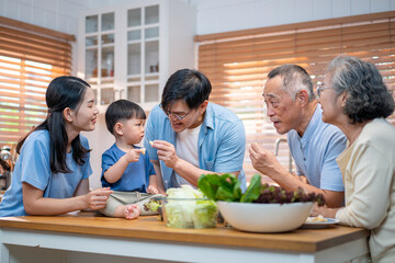 Asian family spending quality time together in the kitchen, preparing healthy meals with fresh vegetables while bonding with their toddler. Promotes family love, nutrition, and home life.