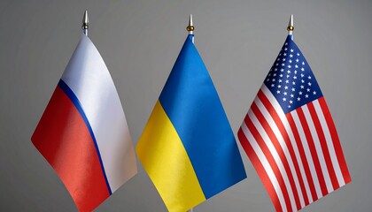Flags of Russia, Ukraine, and United States displayed vertically on flagpoles against neutral gray background, symbolizing national identity, diplomatic tension, and global political dynamics.