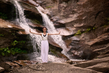 woman performing slow tai chi movements near a waterfall and river at sunset capturing harmony balance and fitness in nature