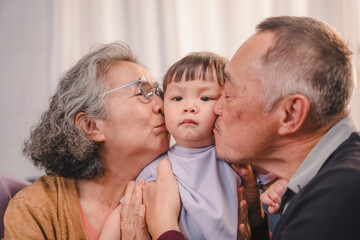 Adorable Asian toddler being kissed on both cheeks by loving grandparents at home. A touching moment that captures unconditional love, emotional bonding, and multigenerational connection.
