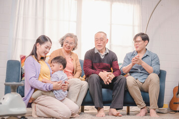 Asian multigenerational family spending quality time together at home. Mother hugging toddler with love while others smile and clap, showing strong emotional family connection.