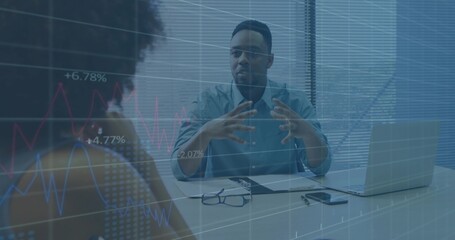 Gesturing man in light blue shirt discussing data at conference desk, with laptop, floating charts