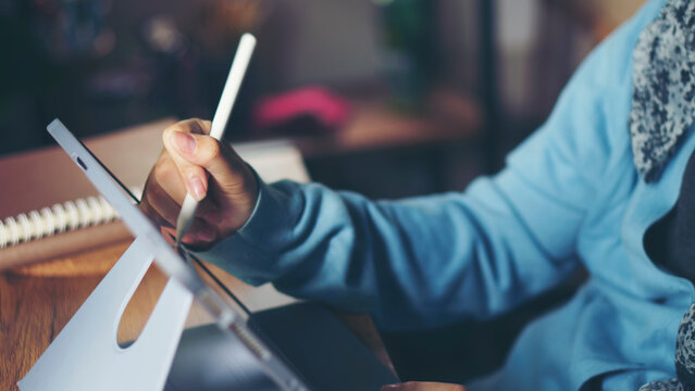 Children hand using digital tablet with stylus pen write and do homework at home. Stress Thai Student working online and reading book to study for the exam. Education and E-learning concept.
