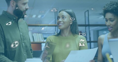Collaborating colleagues using tablet, papers, laptop at desk with books, eco icons