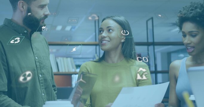 Collaborating colleagues using tablet, papers, laptop at desk with books, eco icons