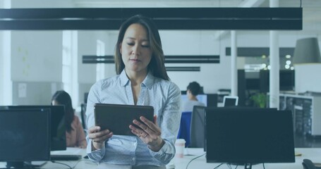 Standing female professional holding tablet and reviewing data in open plan office, with monitors