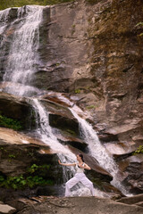 Naklejka premium woman performing slow tai chi movements near a waterfall and river at sunset capturing harmony balance and fitness in nature