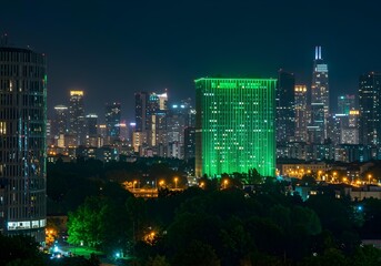 Obraz premium Night cityscape panorama: illuminated skyscrapers, green building, urban park, modern architecture, vibrant city lights.