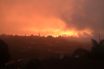 Fototapeta premium Dramatic fiery sunset sky with vibrant orange and red hues illuminating a silhouetted treeline and distant landscape