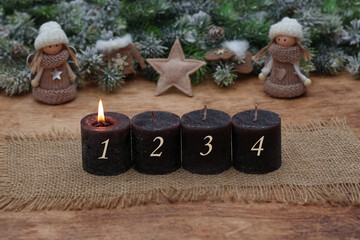 First Advent: Brown candles with numbers arranged in front of fir branches and winter dolls.