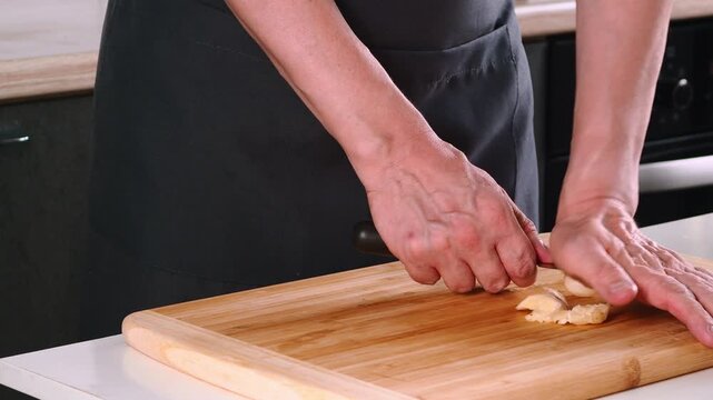 A person is skillfully chopping garlic on a wooden cutting board. The kitchen has a contemporary design with sleek appliances and a focus on culinary preparation
