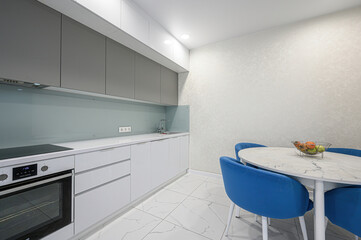 modern kitchen with white cabinets, marble floor, and a round table with blue chairs. Fruit bowl adds a splash of color