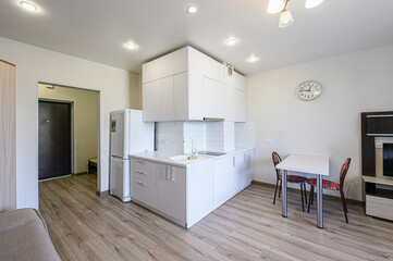 bright, modern kitchen and dining area with white cabinets, appliances, and a small table with two chairs. The flooring is light wood