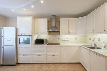 well-lit kitchen featuring white cabinets, a stainless steel refrigerator, an oven, a microwave, and a sink. The floor is tiled in a warm brown tone