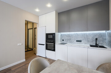 Modern kitchen with white cabinets, gray upper cabinets, marble backsplash, and wood floors. A minimalist, clean design
