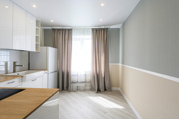 Fototapeta premium Bright kitchen featuring white cabinets, wooden countertops, a large sink, and a window with beige curtains, and a two-tone gray and beige wall