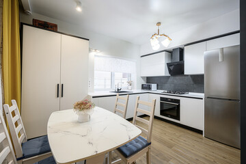 modern kitchen featuring white cabinets, a marble-patterned table with wooden chairs, and stainless steel appliances